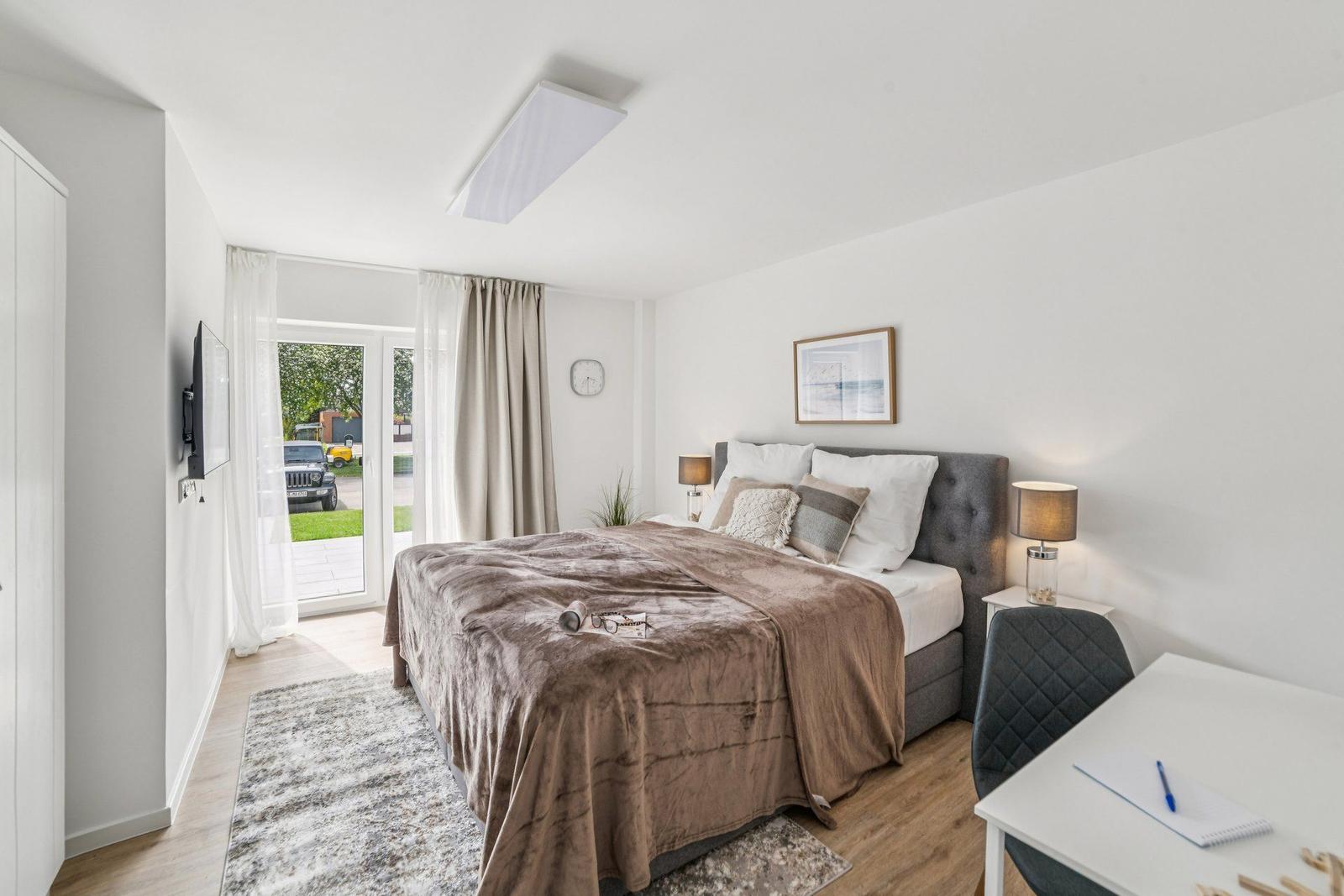 Schlafzimmer mit Bett, Schreibtisch und Glasfront zur Terrasse.