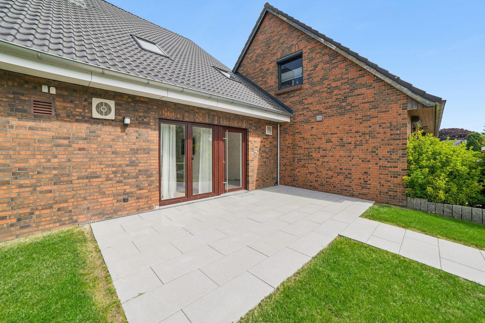 Haus mit Backsteinfassade, Terrasse und grünem Gartenbereich.