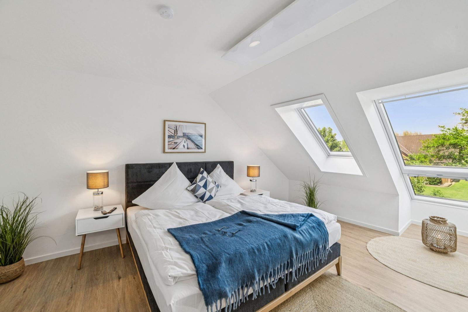 Schlafzimmer mit Dachfenstern, Bett, Nachttischen und Pflanzen.