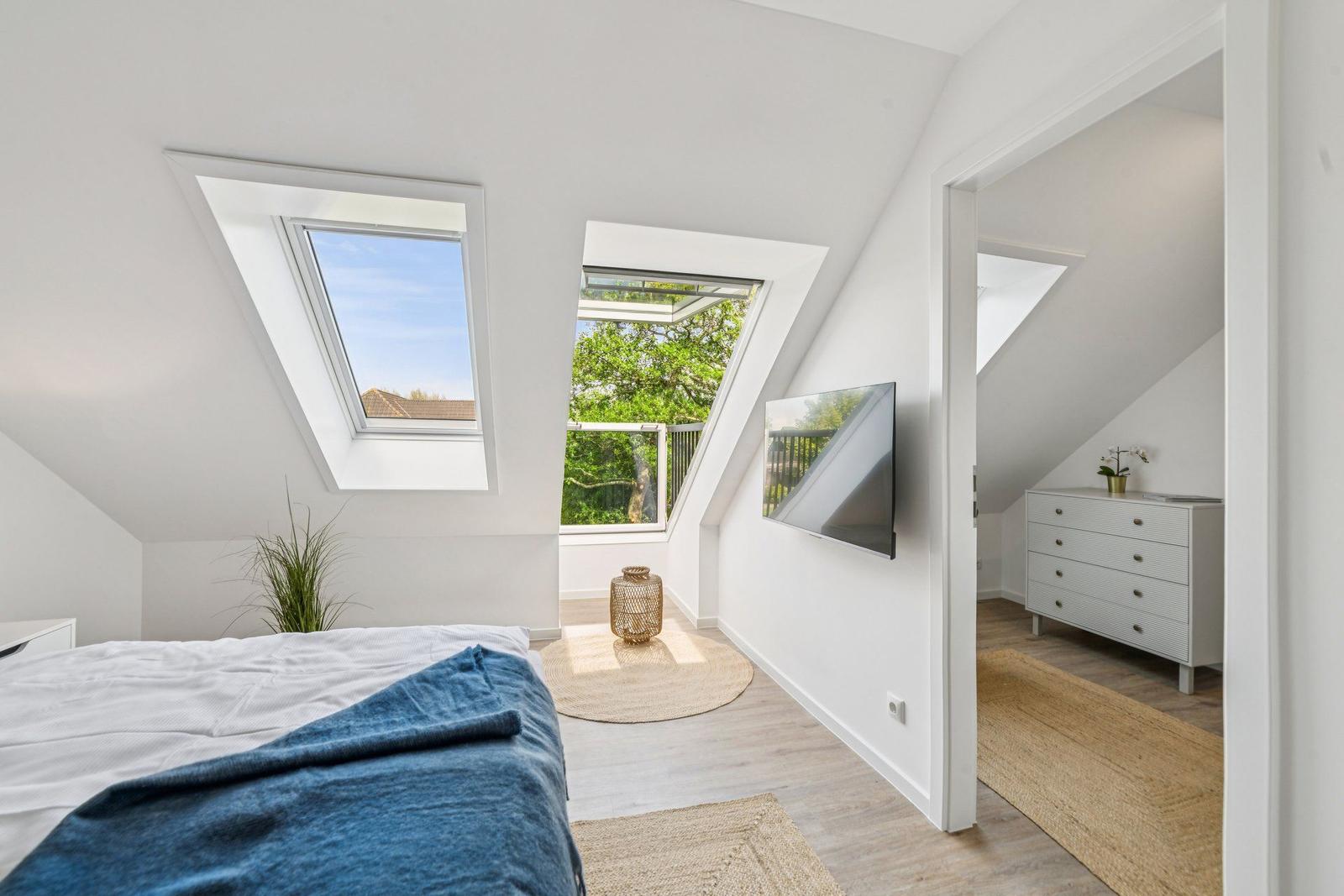 Schlafzimmer mit Dachfenstern, TV und Blick auf Balkon