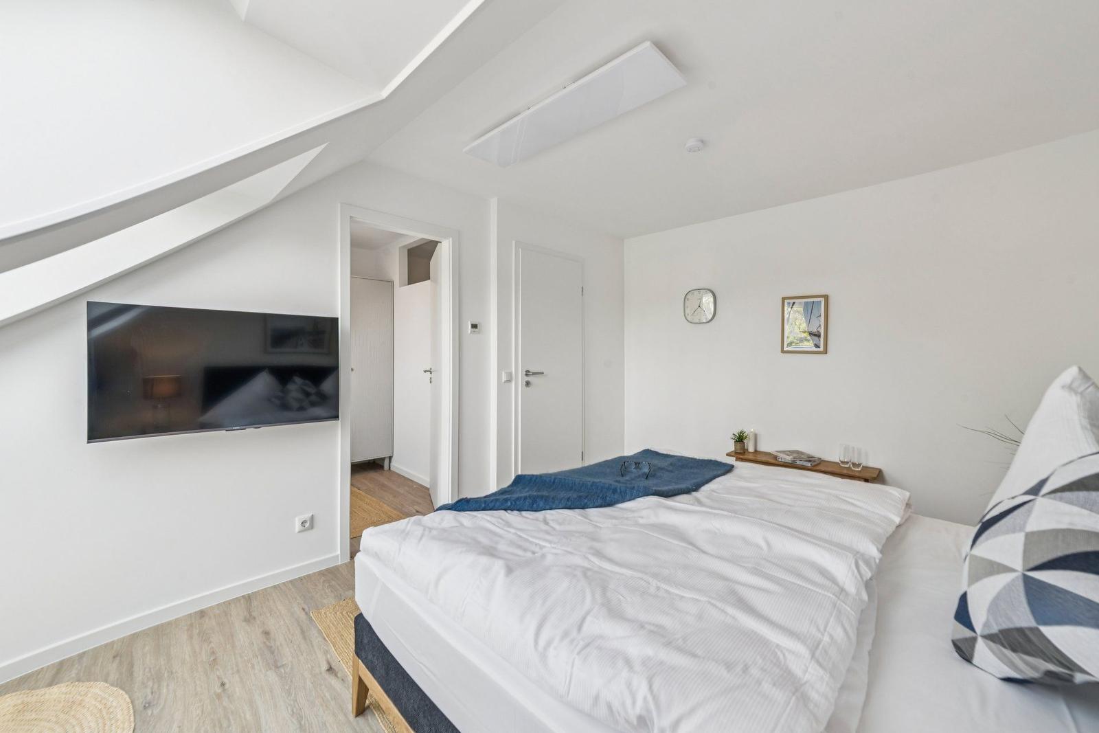 Schlafzimmer mit Bett, Fernseher und Holzboden