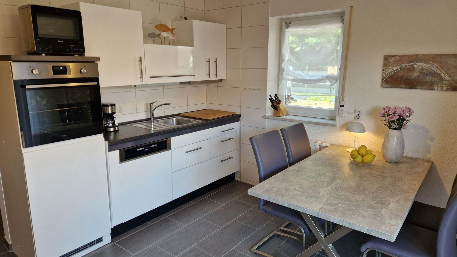 Küche mit Essbereich, weißen Schränken, Herd und Tisch mit Stühlen.