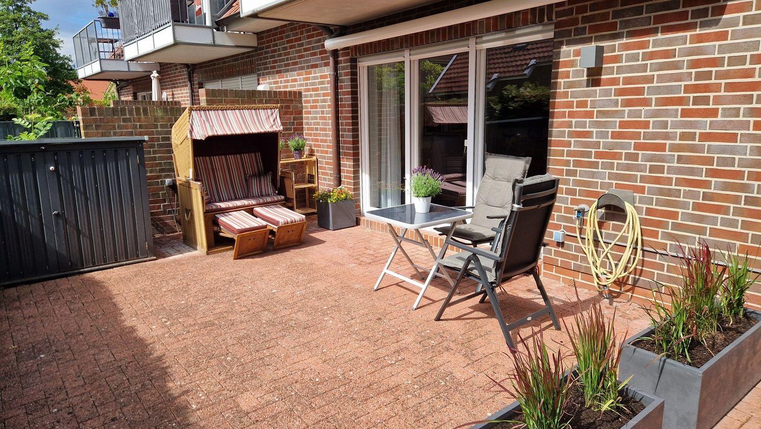 Terrasse mit Liegestuhl, Tisch und Stühlen. Pflanzen und Ziegelsteinbelag.