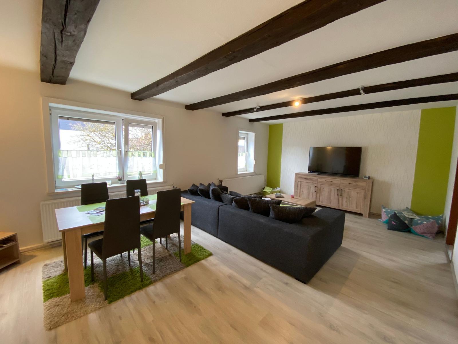 Wohn- und Essbereich mit Holzbalken, Sofa, TV und Tisch mit Stühlen.
