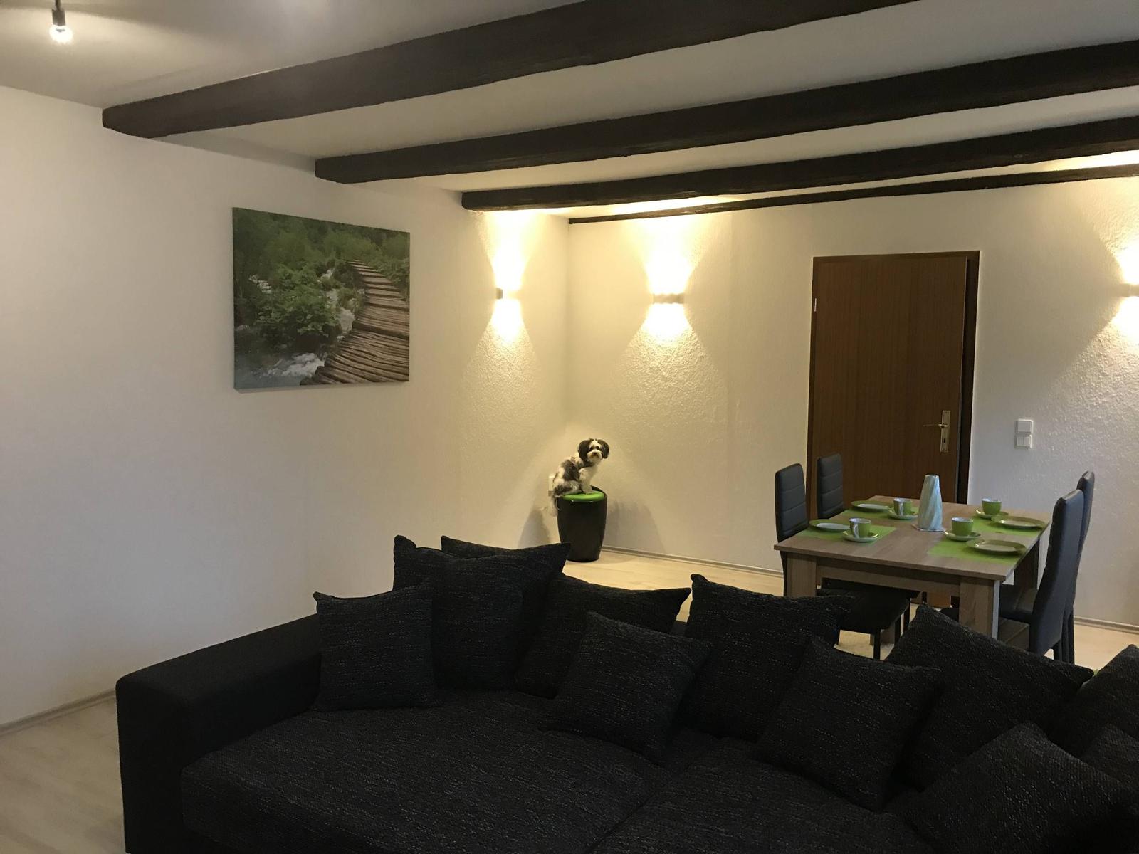 Wohn- und Essbereich mit Sofa, Tisch und Wandbild. Holzbalken an der Decke.