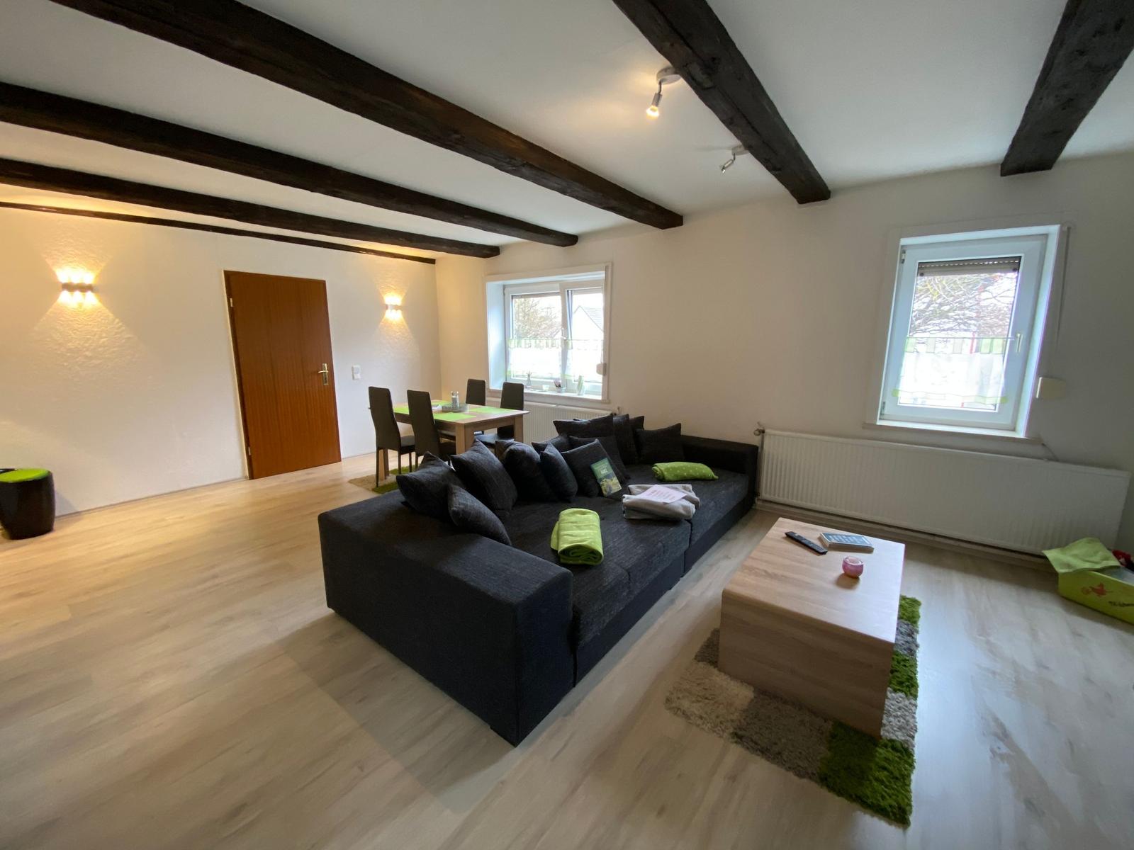 Wohnzimmer mit Sofa, Couchtisch und Essbereich unter Balkendecke.