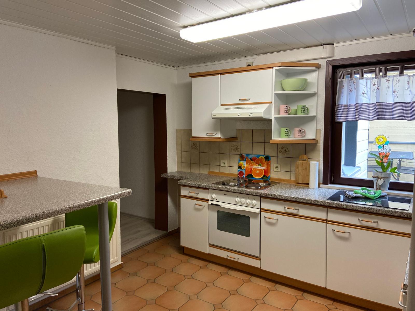 Küche mit weißen Schränken, Arbeitsplatte und Fenster mit Vorhang.