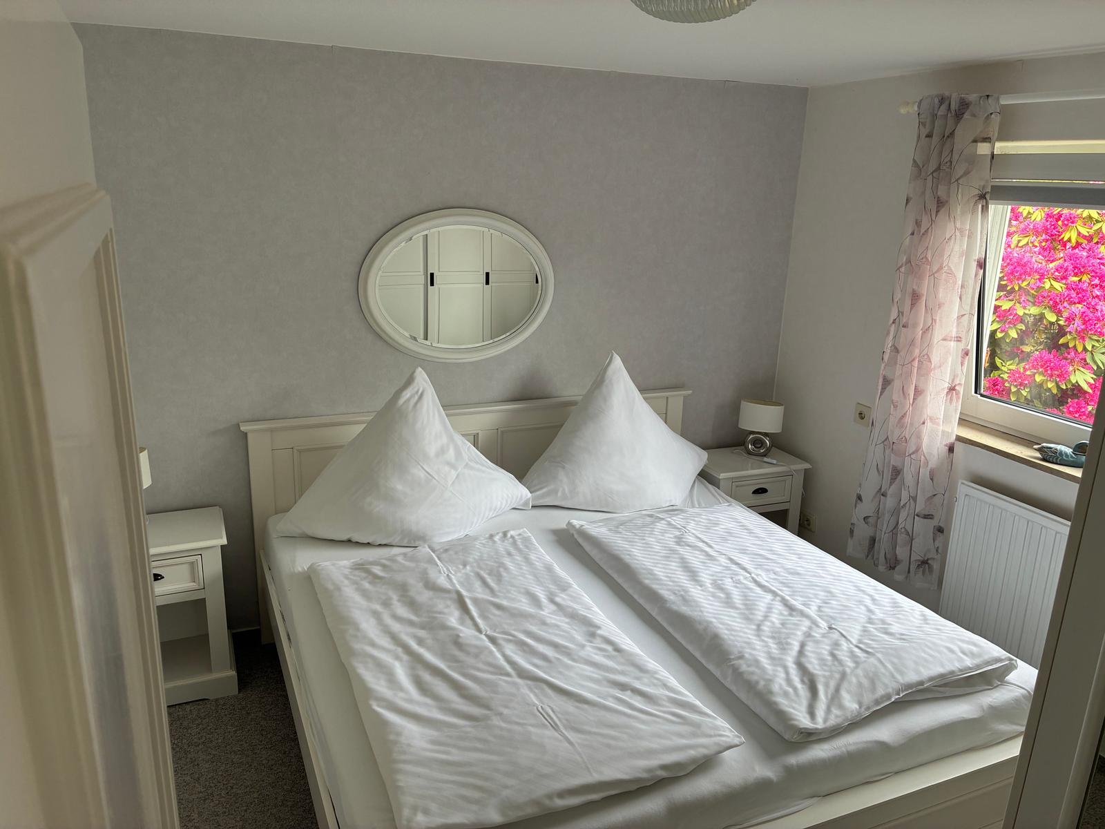 Schlafzimmer mit Doppelbett, Nachttischen und Fenster mit Blick auf Blumen.