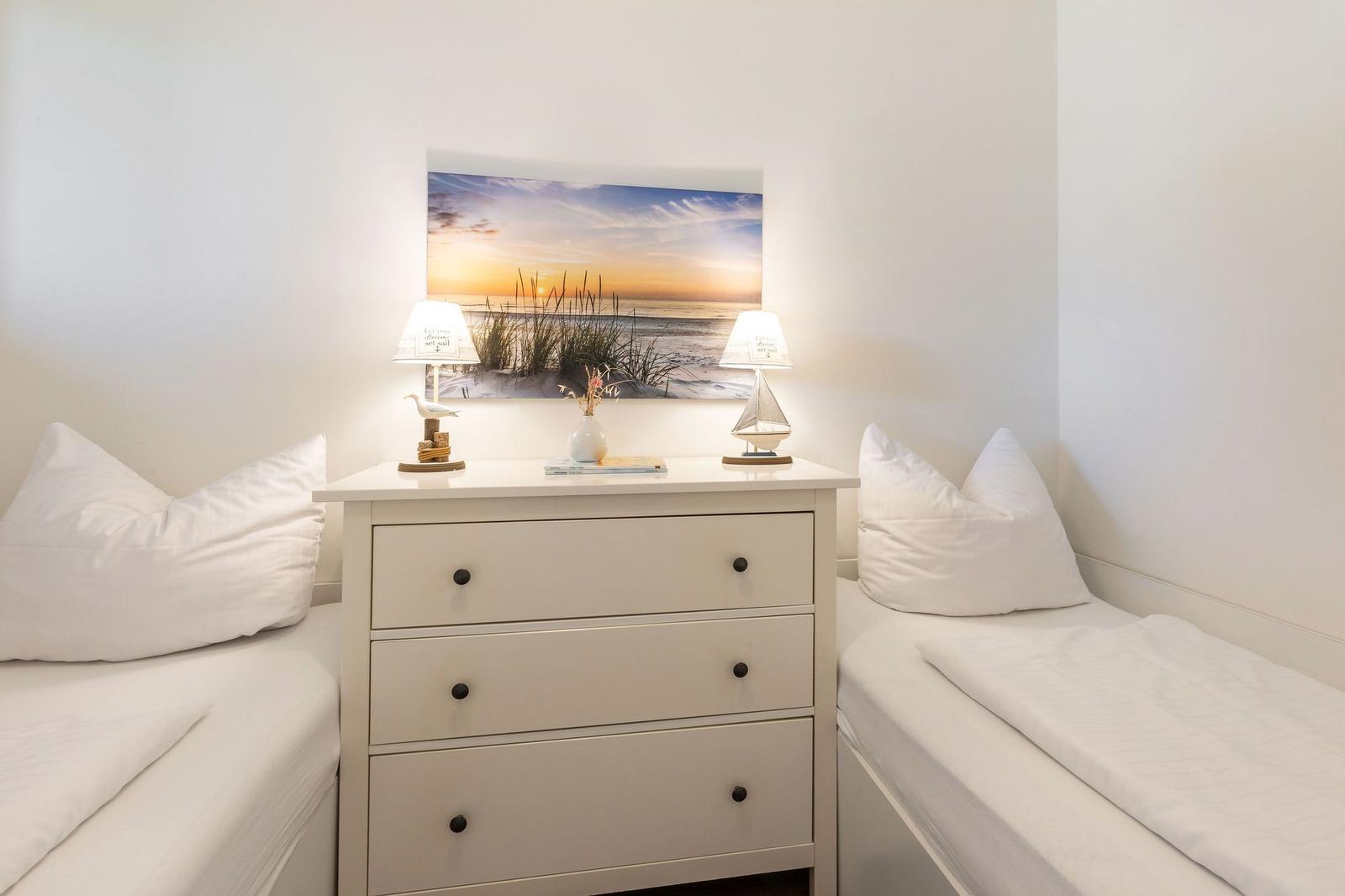 Zwei Betten flankieren einen Schrank mit Lampen und Bild.