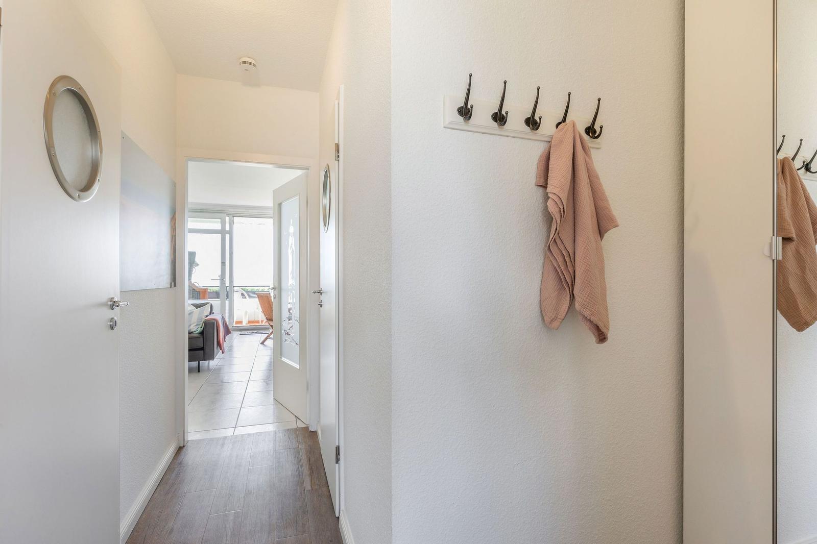 Flur mit Hakenwand, rosa Handtuch und Blick in Wohnbereich mit Terrasse.