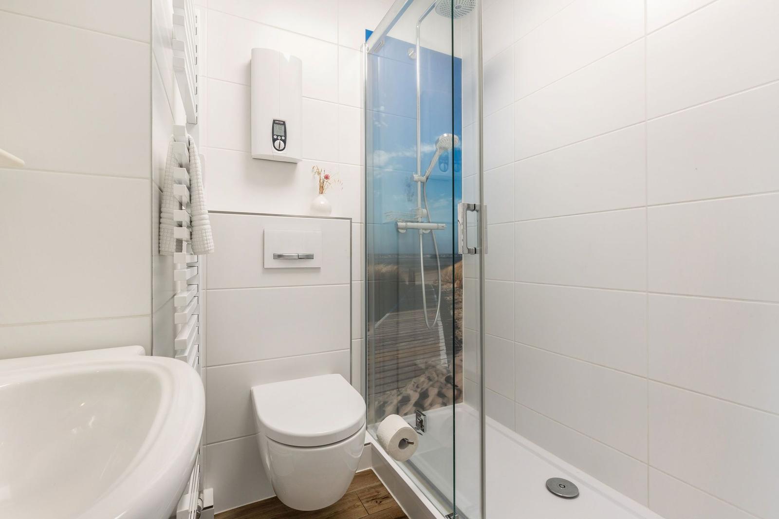 Badezimmer mit Dusche, Toilette und Waschbecken. Weiße Fliesen und Holzboden.