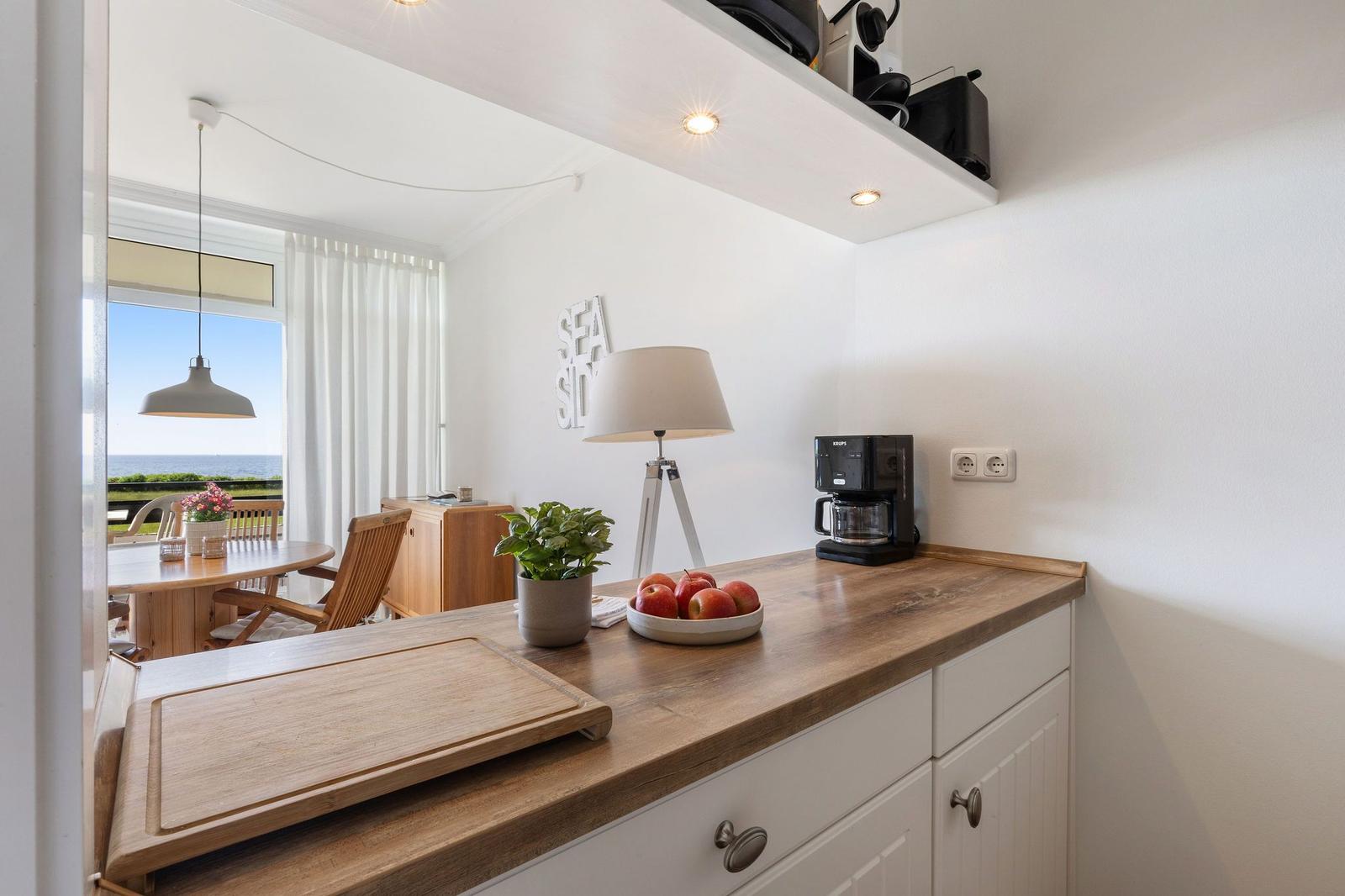 Küchenbereich mit Holzoberfläche, Kaffeemaschine und Obstschale. Blick auf Terrasse und Meer.