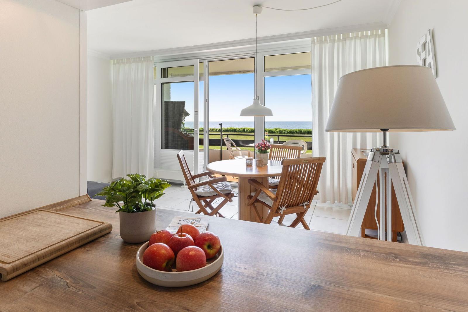 Küche mit Blick auf Terrasse und Meer. Tisch, Stühle und Lampe sichtbar.