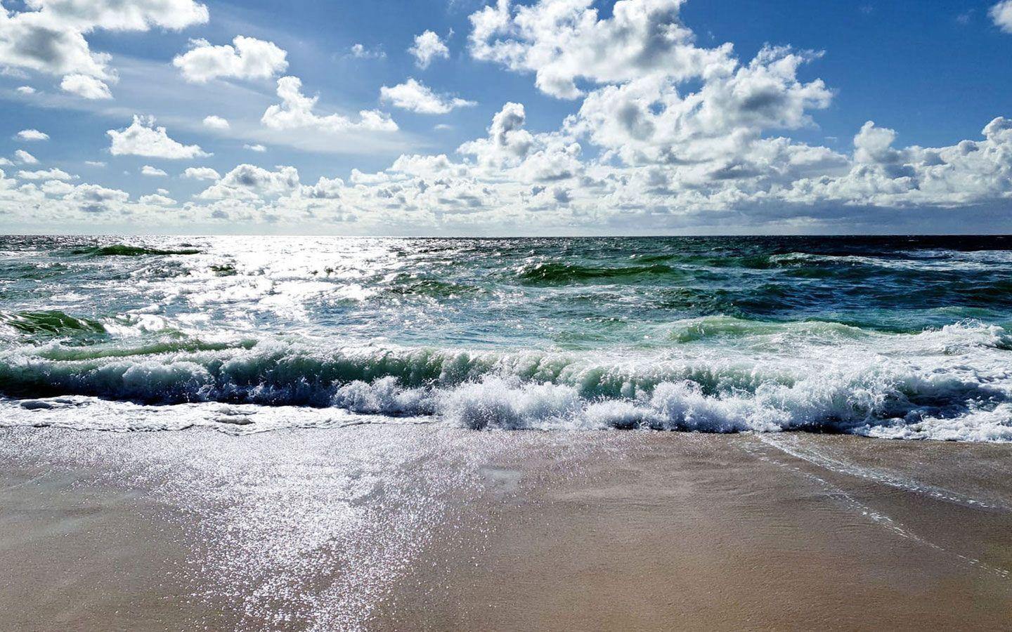 Wellen brechen an einem sandigen Strand unter einem bewölkten Himmel.