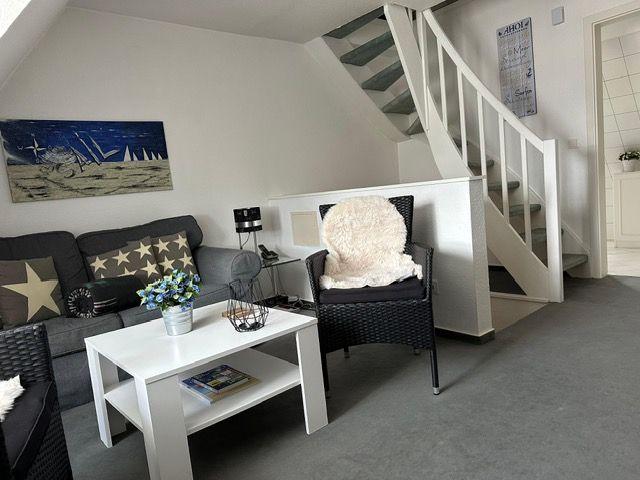 Wohnzimmer mit Sofa, Sessel und Tisch unter Treppe.