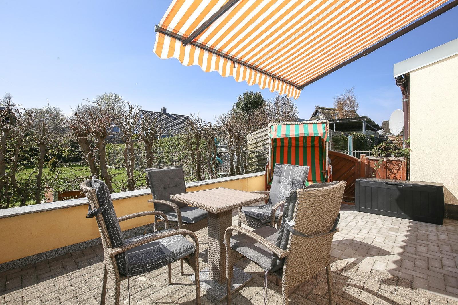 Terrasse mit Sitzgruppe, Sonnenschutz und Blick auf Garten und Nachbarhäuser.