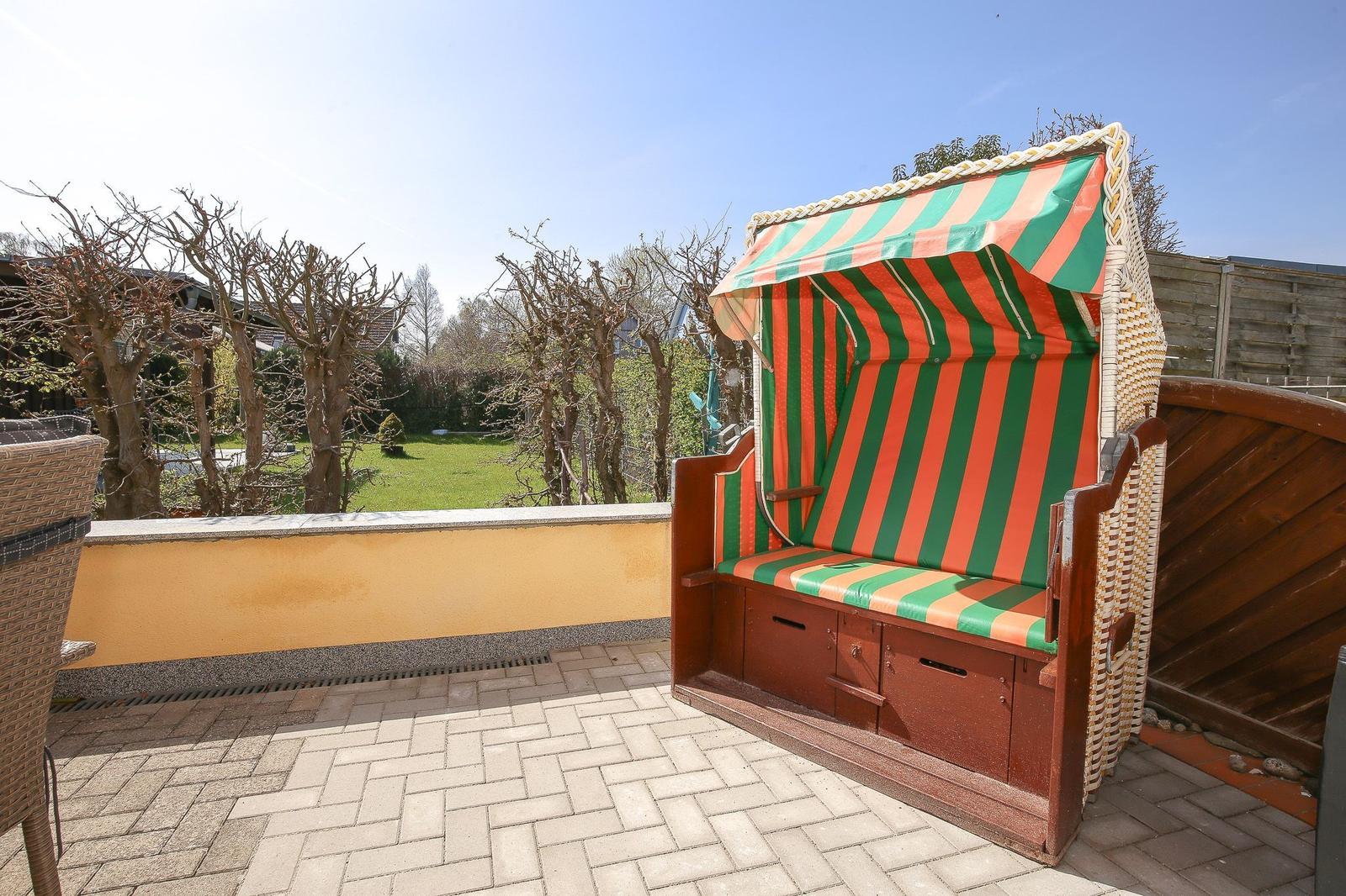 Terrasse mit Strandkorb in grün-orange Streifen, Blick auf Garten und Bäume.