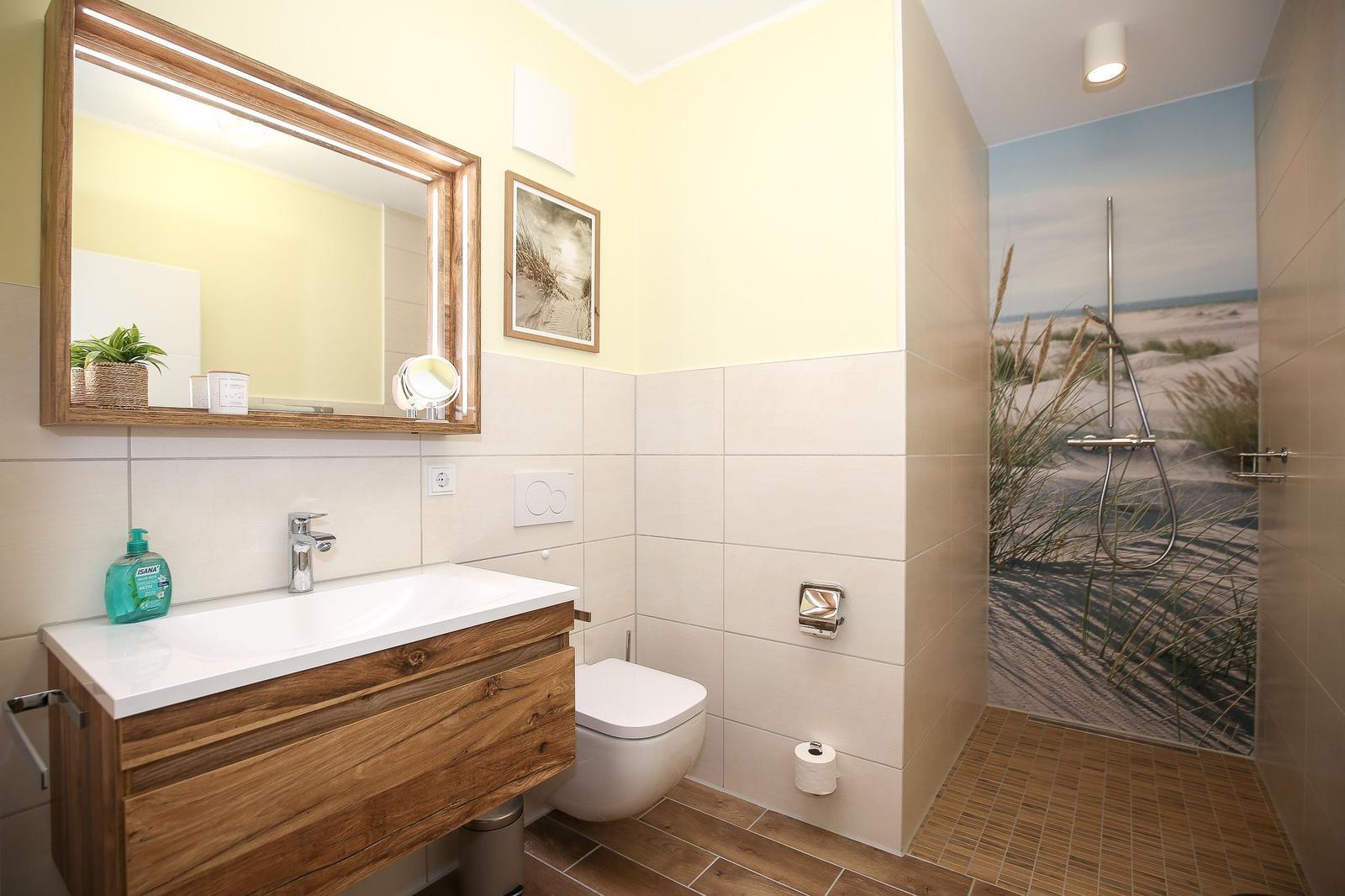 Badezimmer mit Dusche, Waschbecken und Toilette. Duschwand zeigt Strandmotiv.
