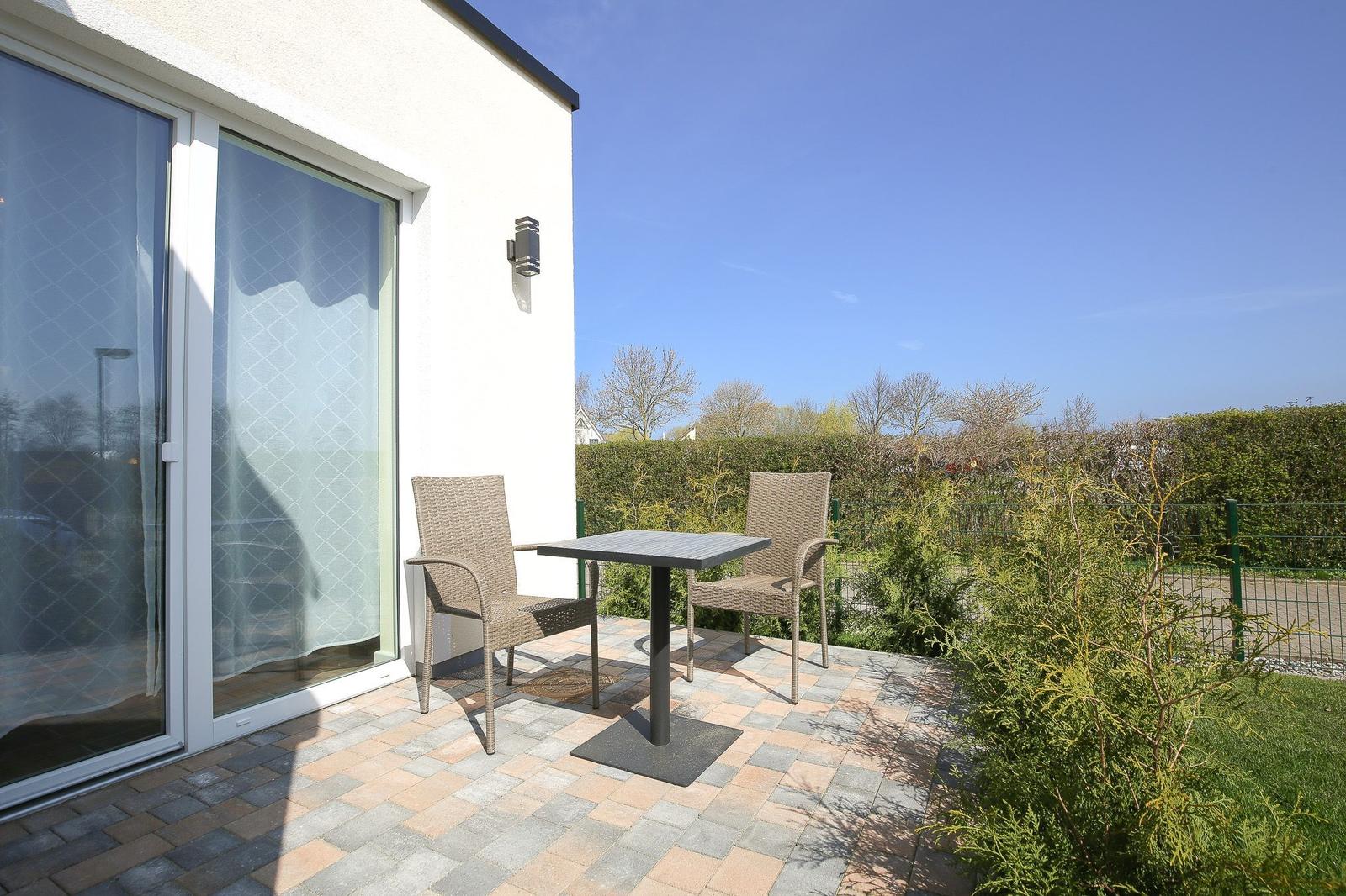 Terrasse mit Tisch und zwei Stühlen vor einer Glasfront.