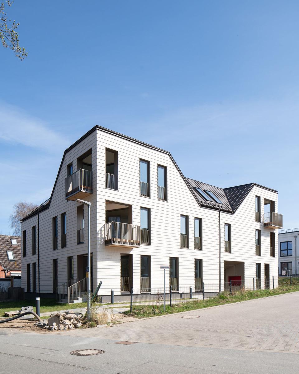 Moderne Wohnhaus mit Balkonen und Dachfenstern unter blauem Himmel.