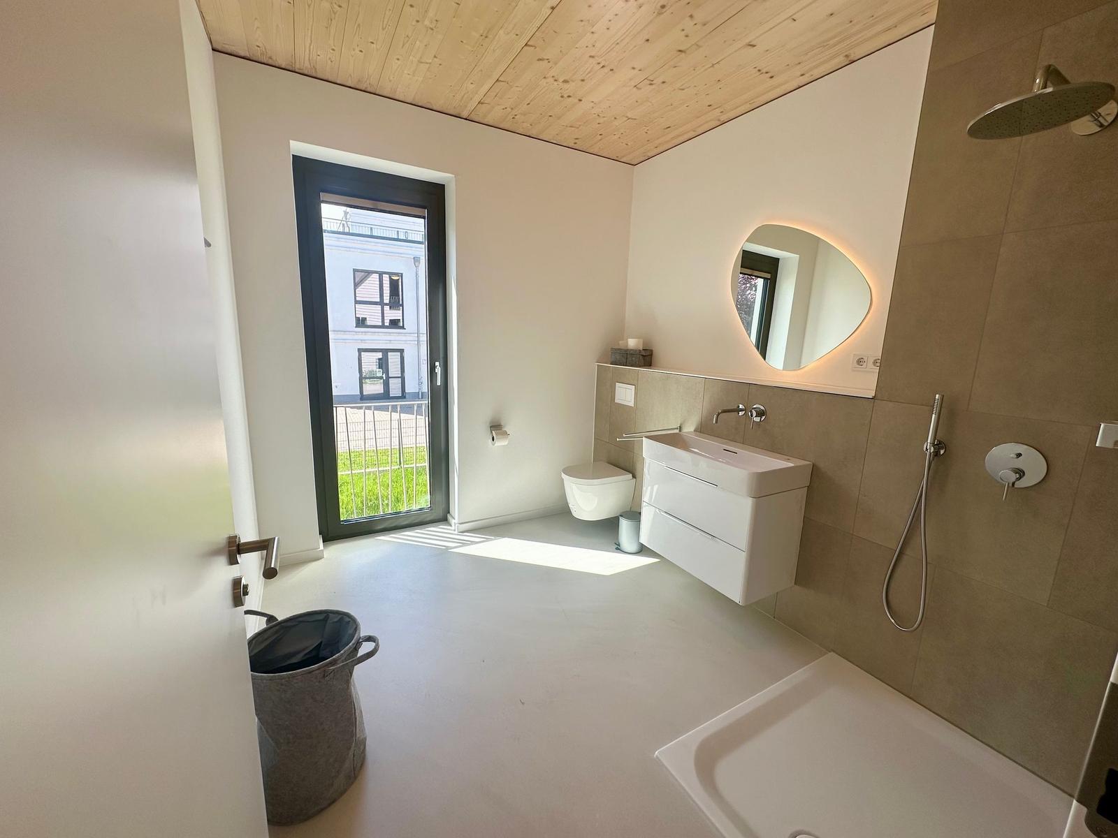 Badezimmer mit Dusche, Waschbecken und Toilette. Holzdecke und Fenster zur Außenterrasse.