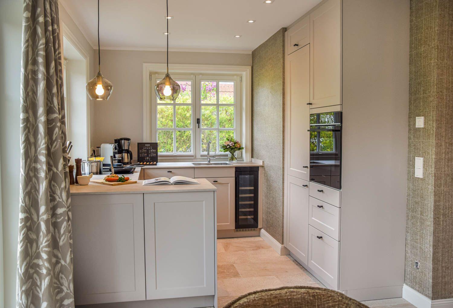 Küche mit weißen Schränken, Fenster, Kühlschrank und Arbeitsplatte.