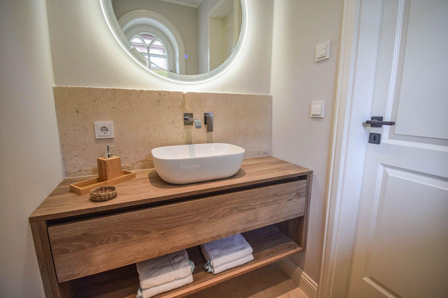 Waschbecken auf Holzkonsole mit Spiegelschrank und Handtuchregal.