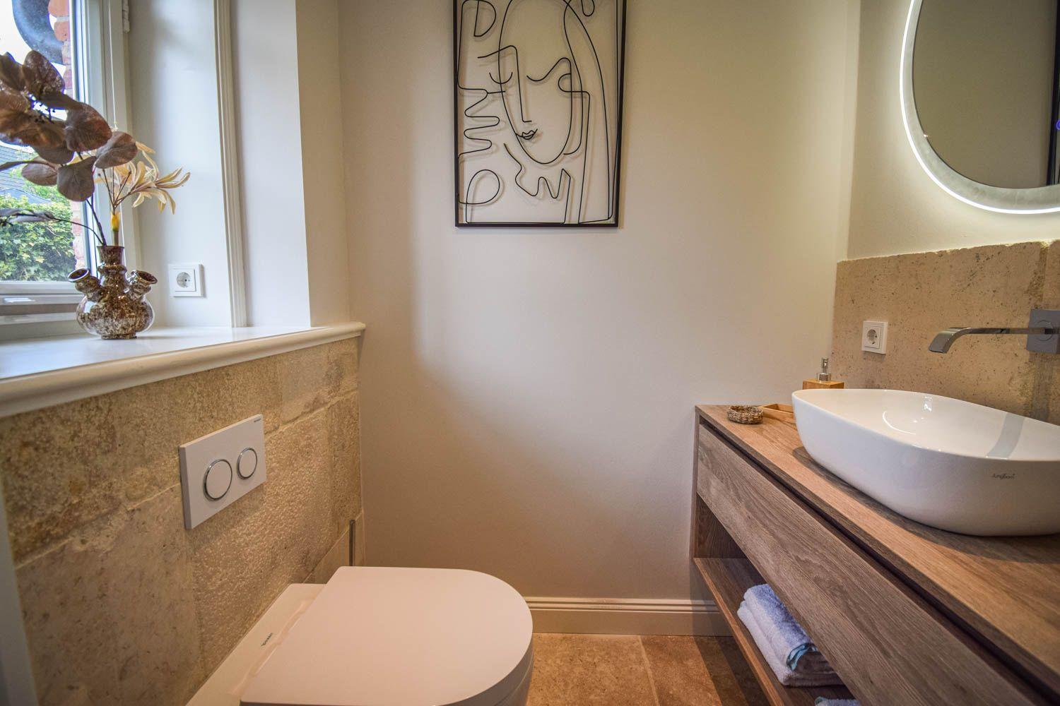 Badezimmer mit Waschbecken, Toilette und Fenster mit Pflanze.