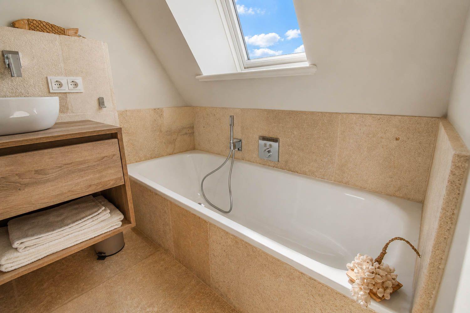 Bad mit Badewanne, Duschkopf und Dachfenster mit Blick auf den Himmel.