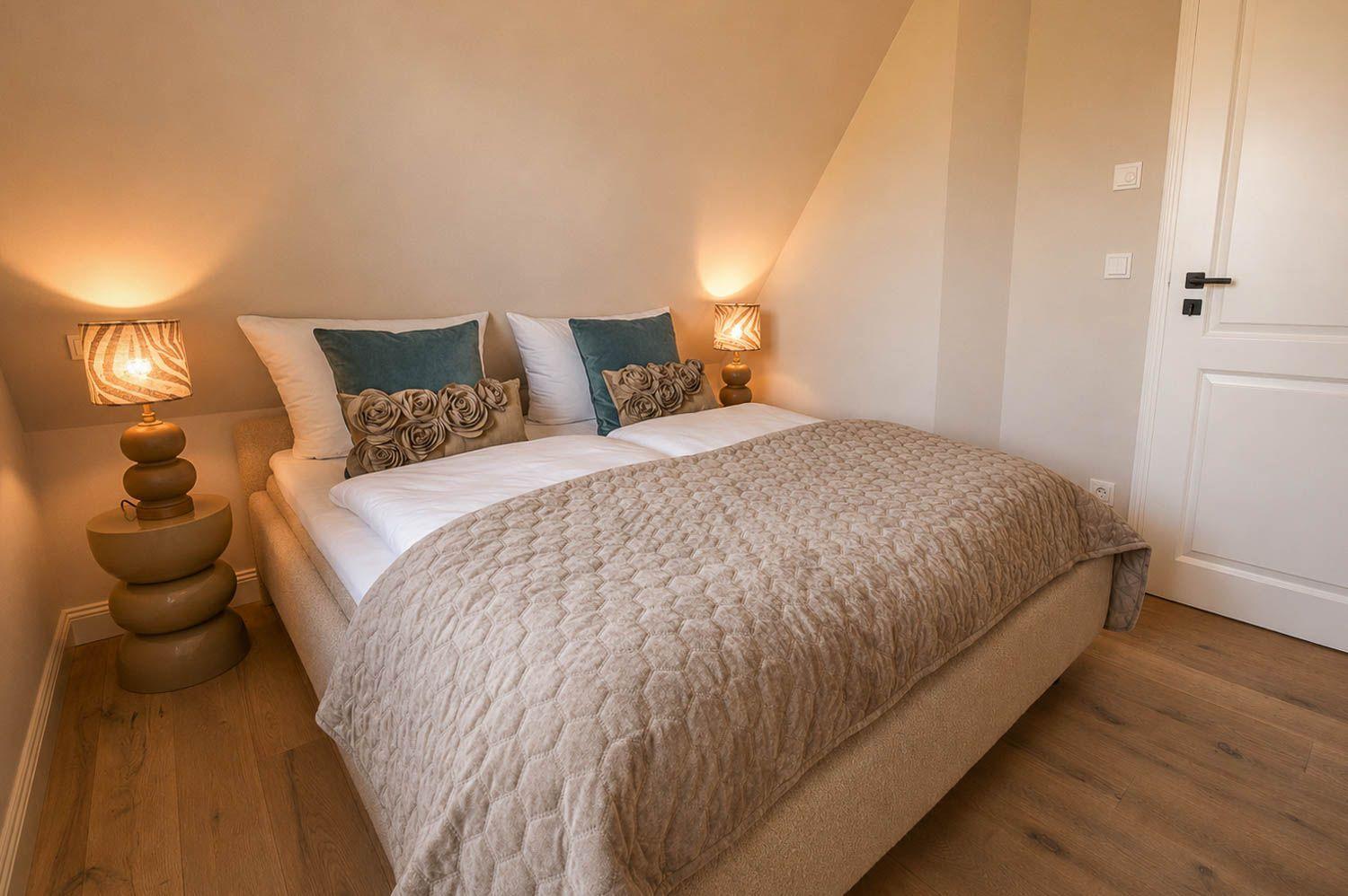 Schlafzimmer mit Bett, zwei Nachttischen und Lampen. Holzboden und weiße Wände.
