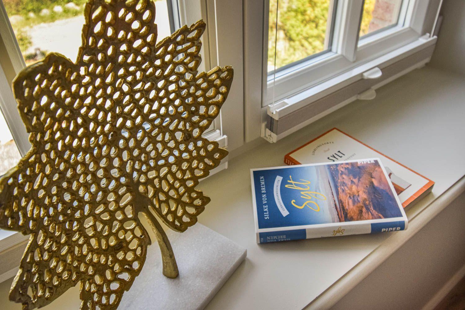 Gelber Blatt-Objekt und Bücher auf Fensterbank mit Blick nach draußen.