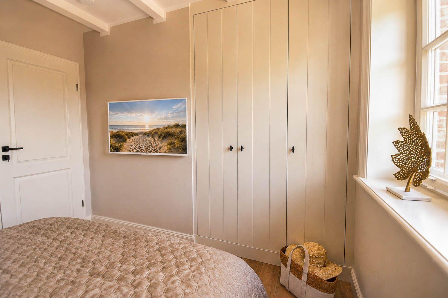 Schlafzimmer mit Bett, Kleiderschrank und Fenster. Wandbild zeigt Strand.