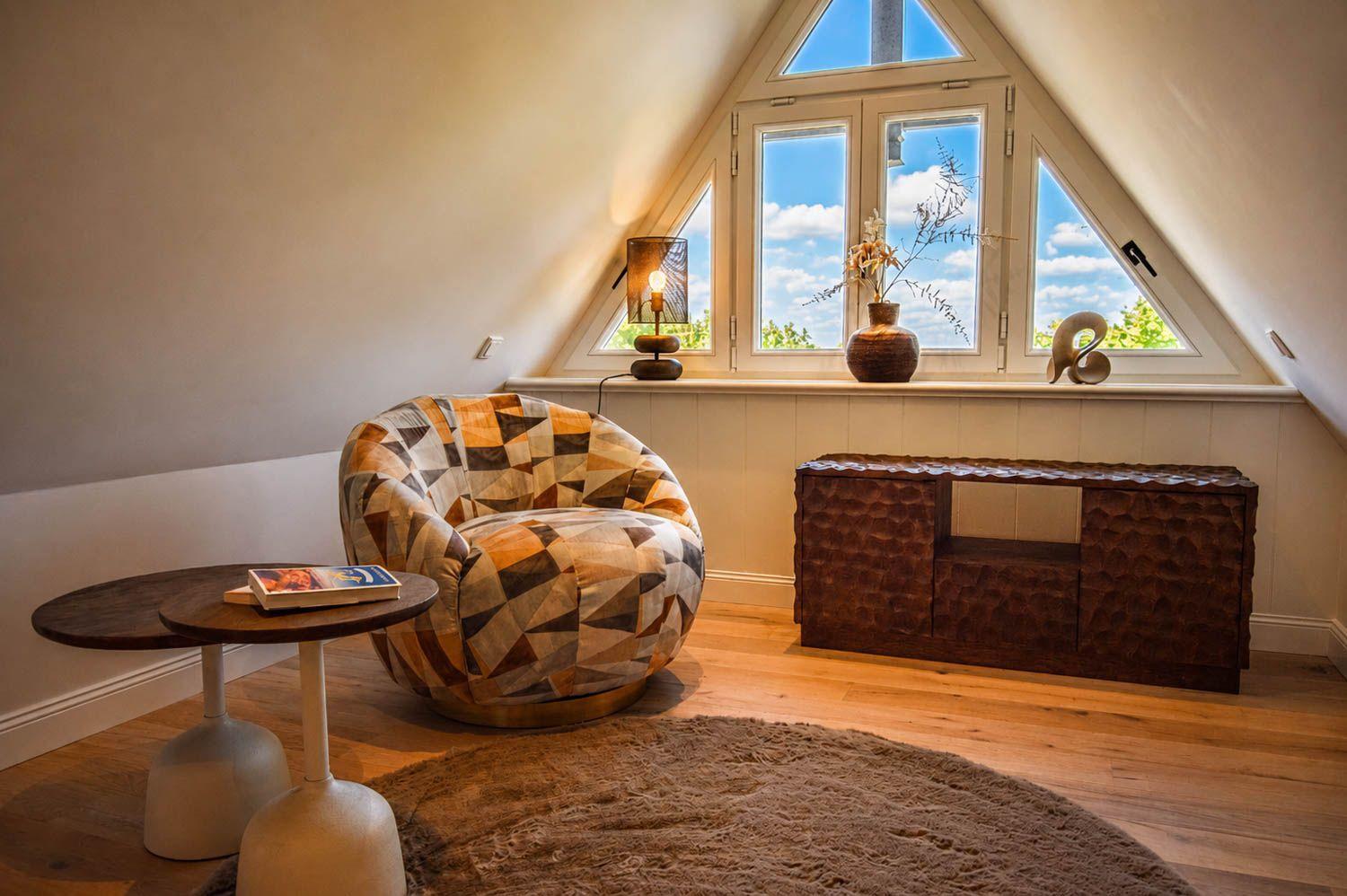 Ein Raum mit einem gemusterten Sessel, einem runden Teppich und einem Fenster mit Blick nach draußen.