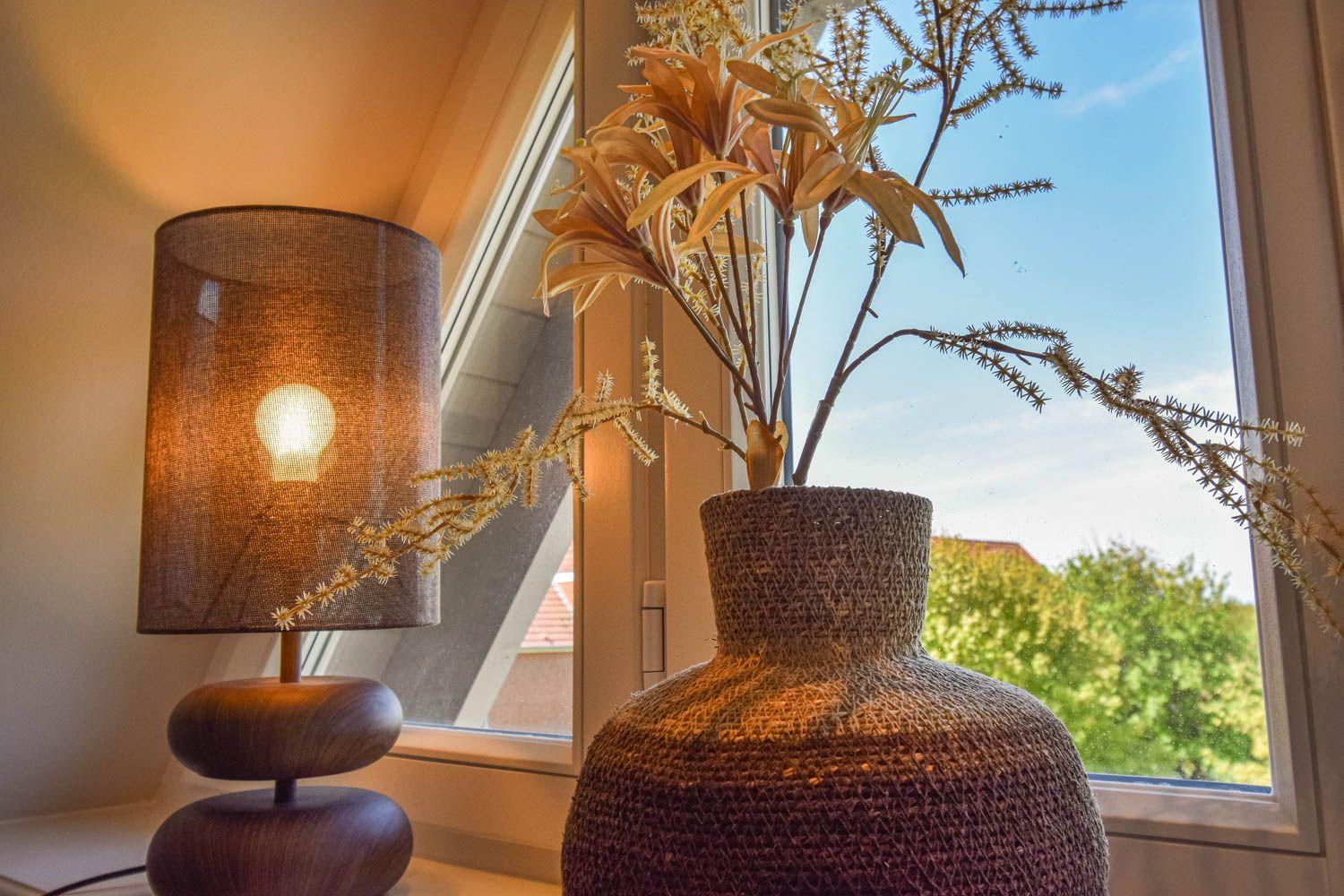Tischlampe und Vasen mit Trockenblumen am Fenster