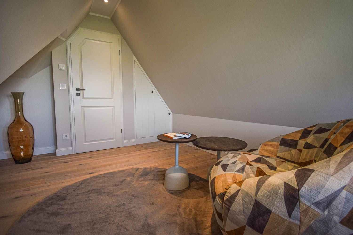 Ein Raum mit schrägen Wänden, Holzboden, Sofa und Tisch.