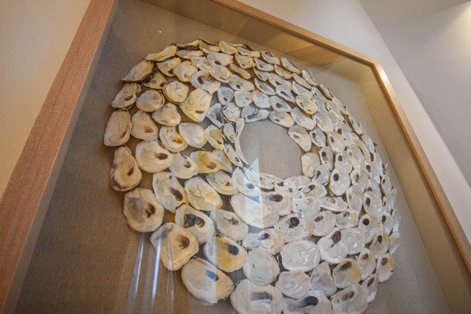 Gefärbtes Kunstwerk aus Muschelschalen in einem Holzrahmen an der Wand.