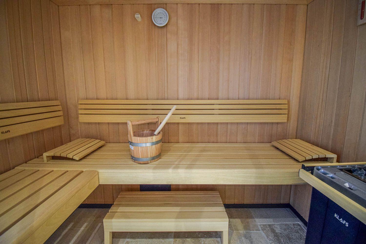 Sauna mit Holzbänken, Eimer und Thermometer an der Wand.