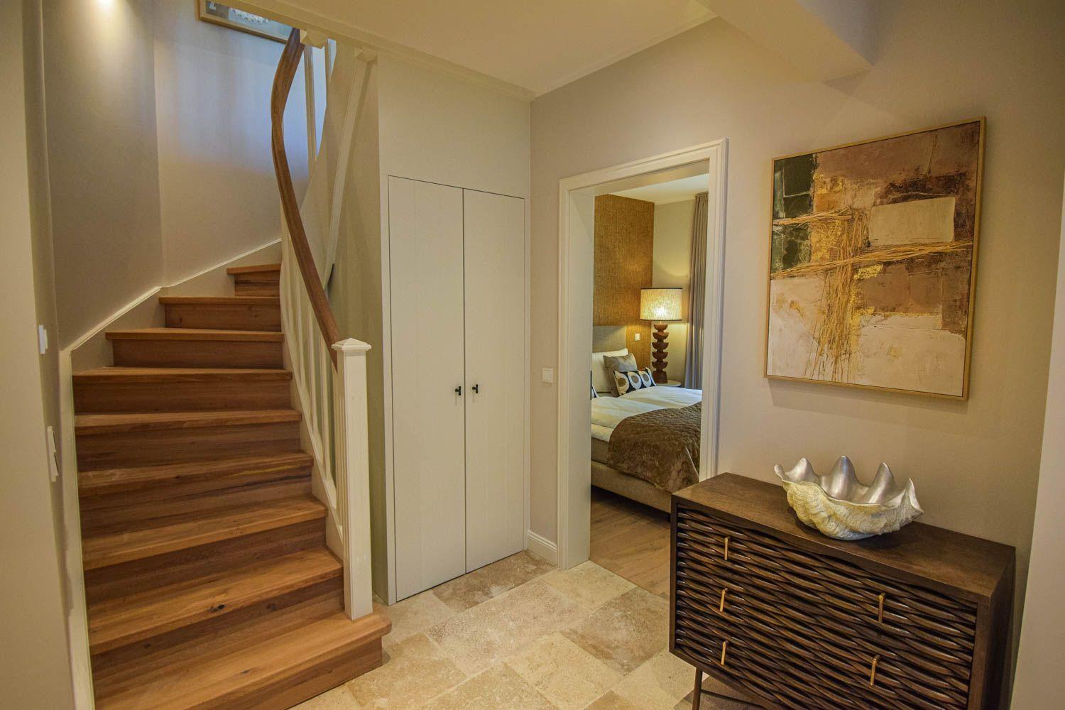 Haus mit Holztreppe, Schrank und Blick in Schlafzimmer mit Bett und Lampe.