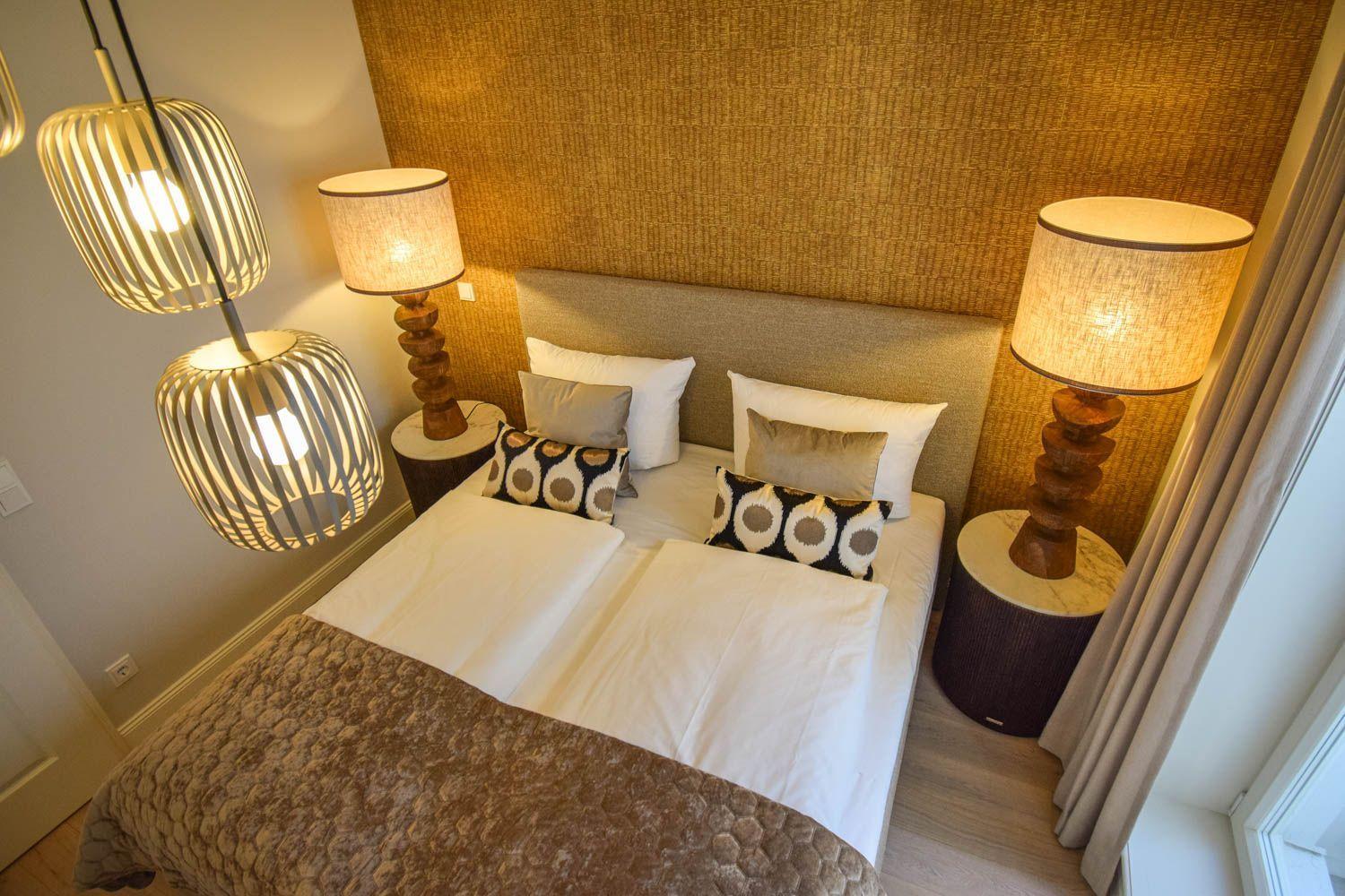 Schlafzimmer mit Bett, zwei Nachttischen und Deckenbeleuchtung. Wandverkleidung und Vorhänge.