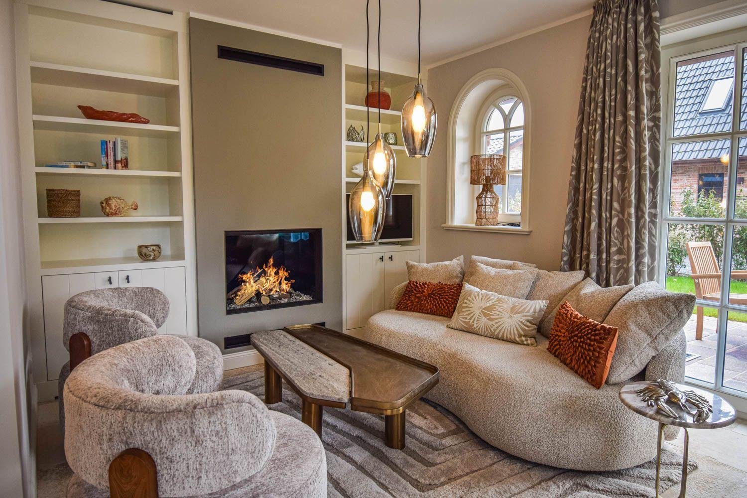 Wohnzimmer mit Kamin, Sofa, Sessel und Glasfront zur Terrasse.