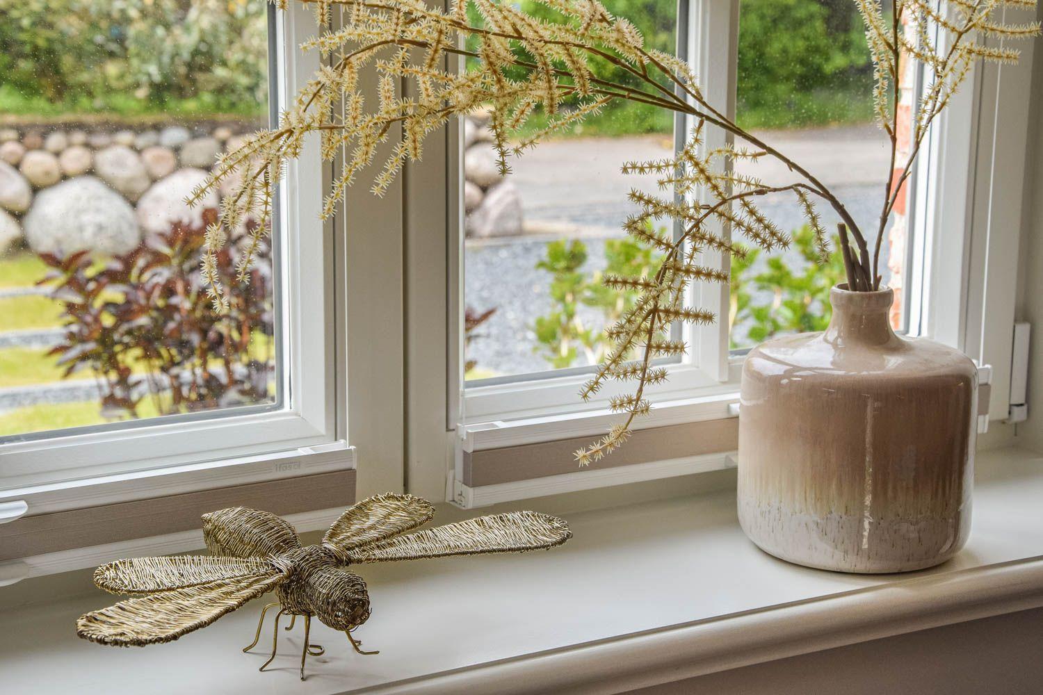 Auf dem Fensterbrett steht eine Vase mit Zweigen und eine geflochtene Libelle.