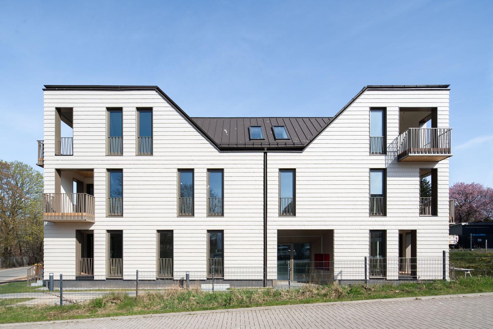 Moderne Mehrfamilienhaus mit Balkonen und Dachfenstern. Außenansicht unter blauem Himmel.