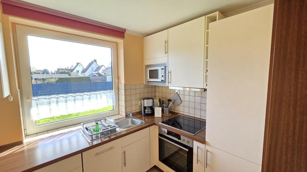 Küche mit Fenster, Spüle, Herd und Mikrowelle. Blick auf Wohngebiet.