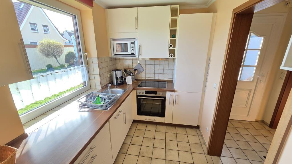 Küche mit Fenster, Spüle, Herd und Mikrowelle. Fliesenboden und weiße Schränke.