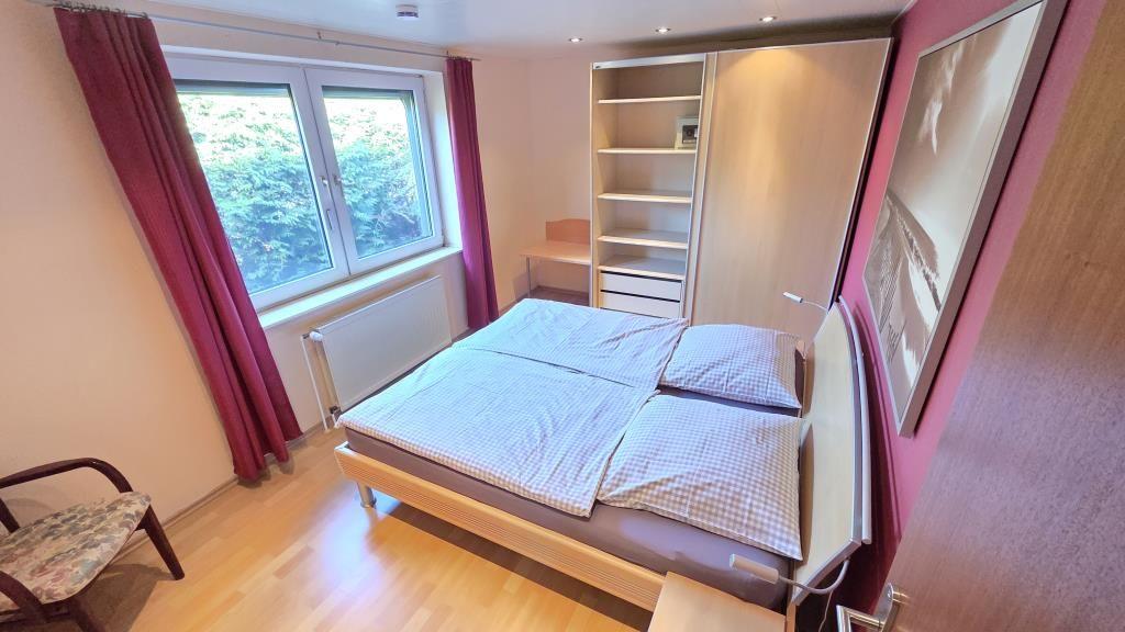 Schlafzimmer mit Doppelbett, Fenster, Schrank und Stuhl.