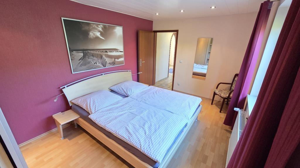 Schlafzimmer mit Doppelbett, Wandbild und Holzboden. Tür führt in einen Flur.