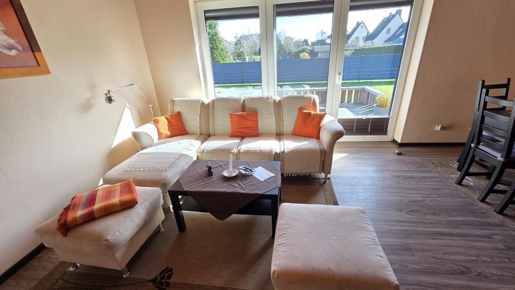 Wohnzimmer mit Sofa, Sitzkissen und Tisch. Durchgang zur Terrasse.