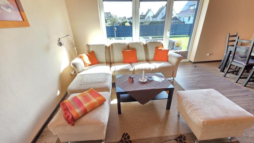 Wohnzimmer mit Sofa, Sitzkissen und Tisch. Durchgang zur Küche und Terrasse.
