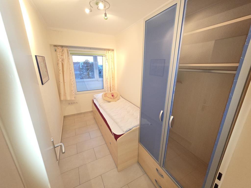 Schlafzimmer mit Einzelbett, Kleiderschrank und Fenster mit Vorhängen.