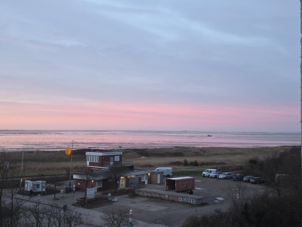 Sonnenuntergang über dem Meer mit Strand und Parkplatz im Vordergrund.